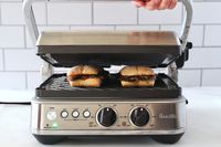 A person lifting the lid of the Breville panini press as it cooks sandwiches.