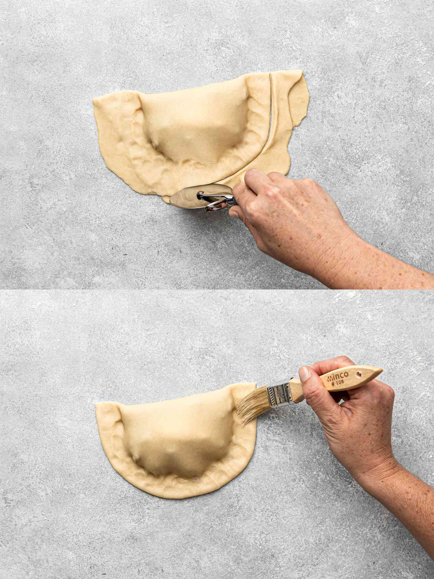 Hands crimping an empanada with a fork, brushing it with a pastry brush.