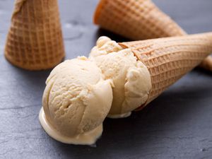 A double scoop of sugar cone ice cream in a sugar cone, arranged on its side on a black slate surface.