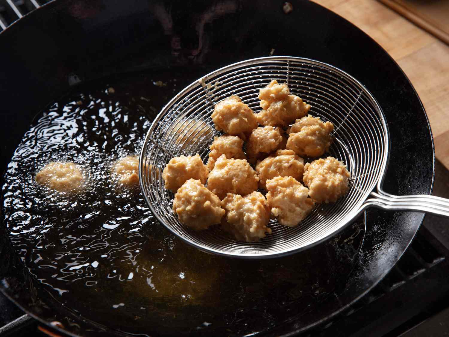 Fried squid balls in a spider being returned to hot oil in a wok for second frying.