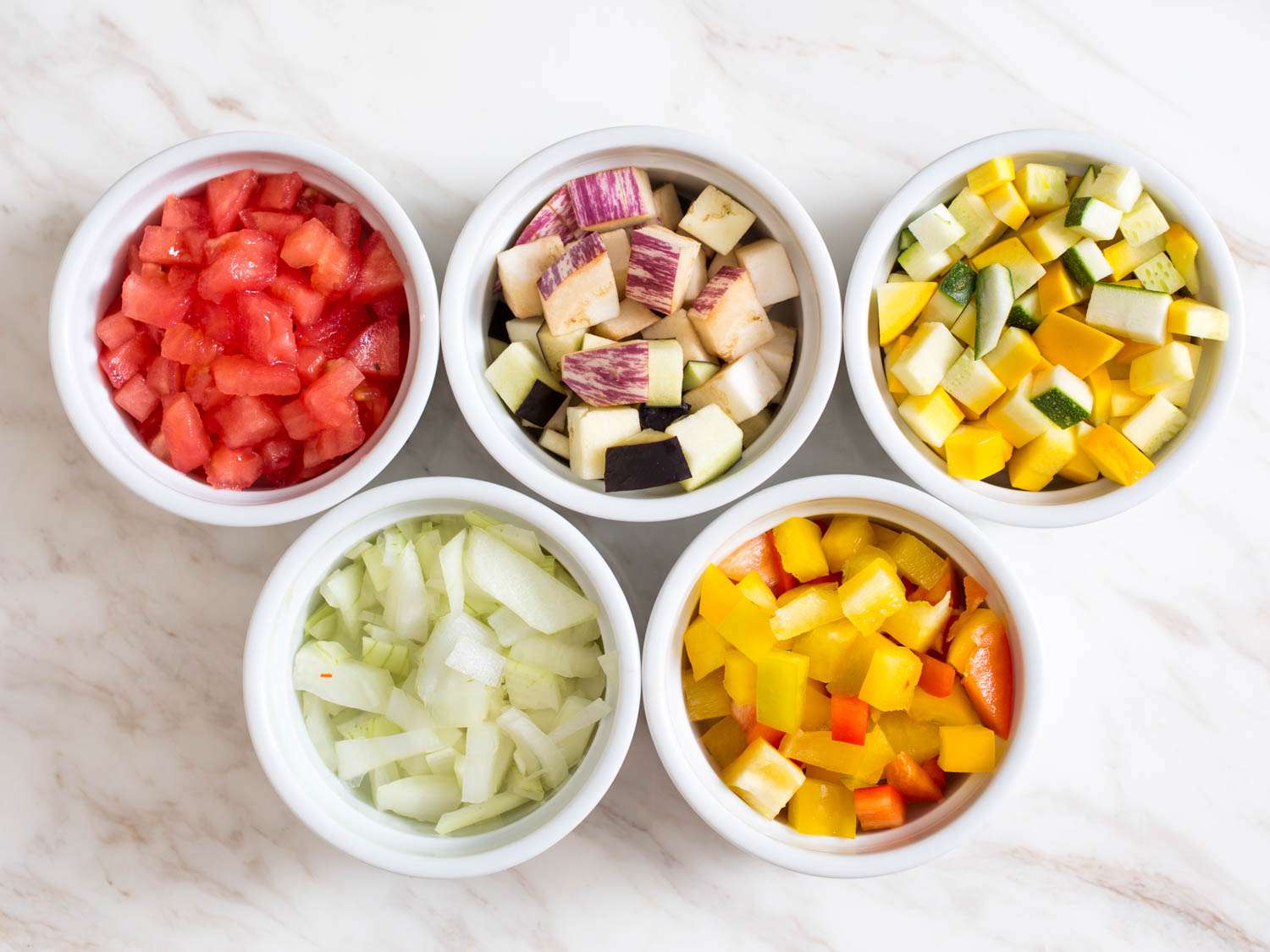 Prep bowls filled with diced tomato, eggplant, squash, onion, and bell pepper. 