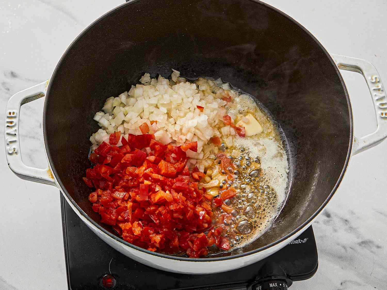 Onions and red peppers cooking in a pot on a stovetop