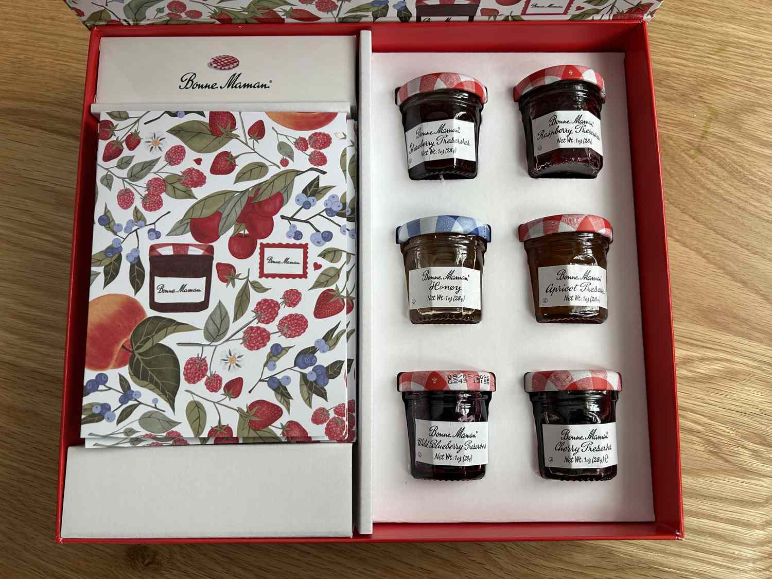 A gift box with a stack of patterned greeting cards and three small jars of jam.