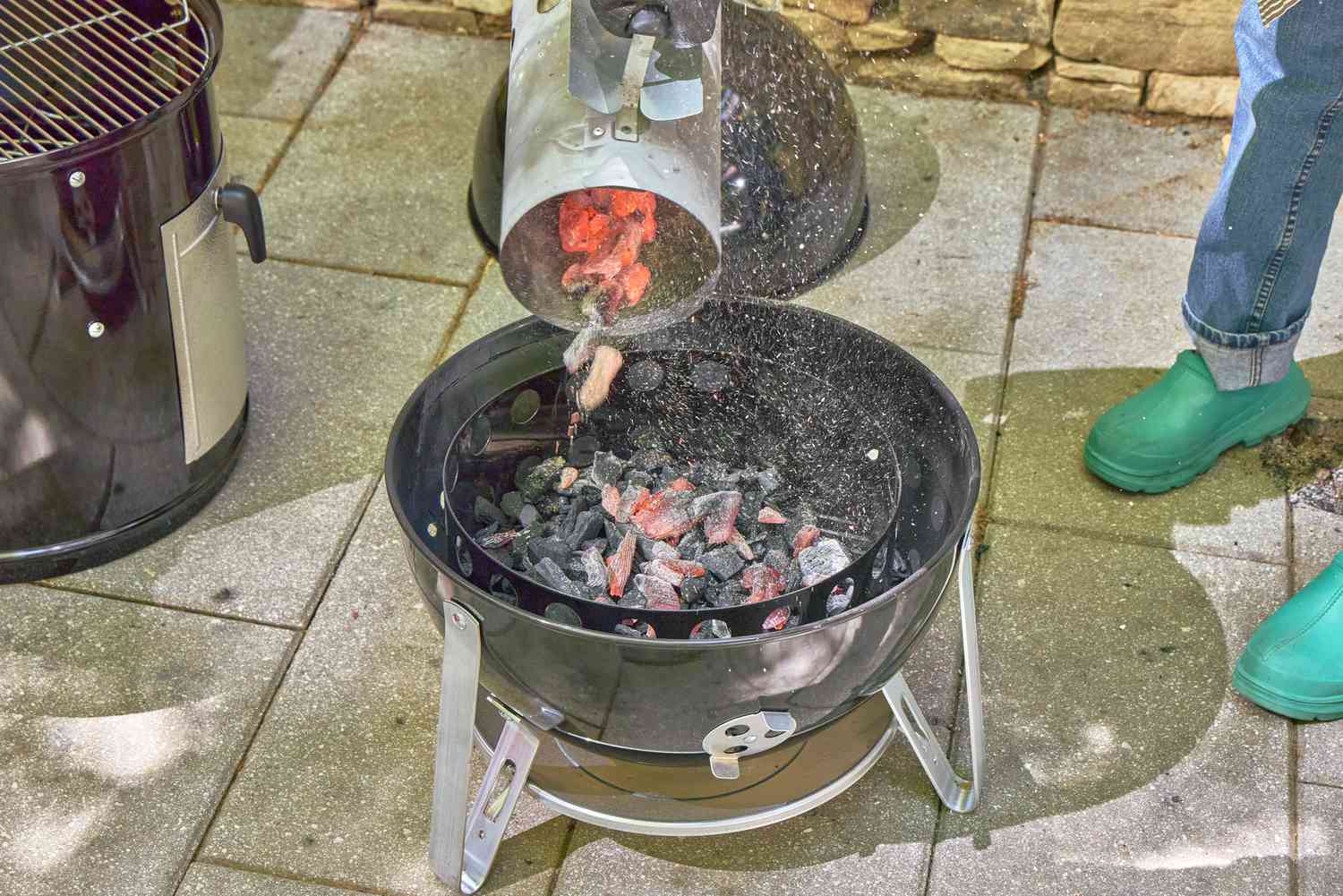 A person pours hot charcoals into the Weber 18-Inch Smokey Mountain Cooker