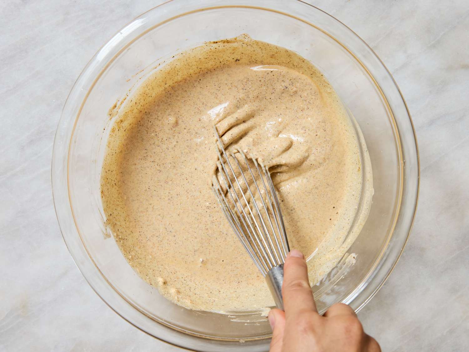 A hand whisking a light mixing bowl filled with a batterlike mixture