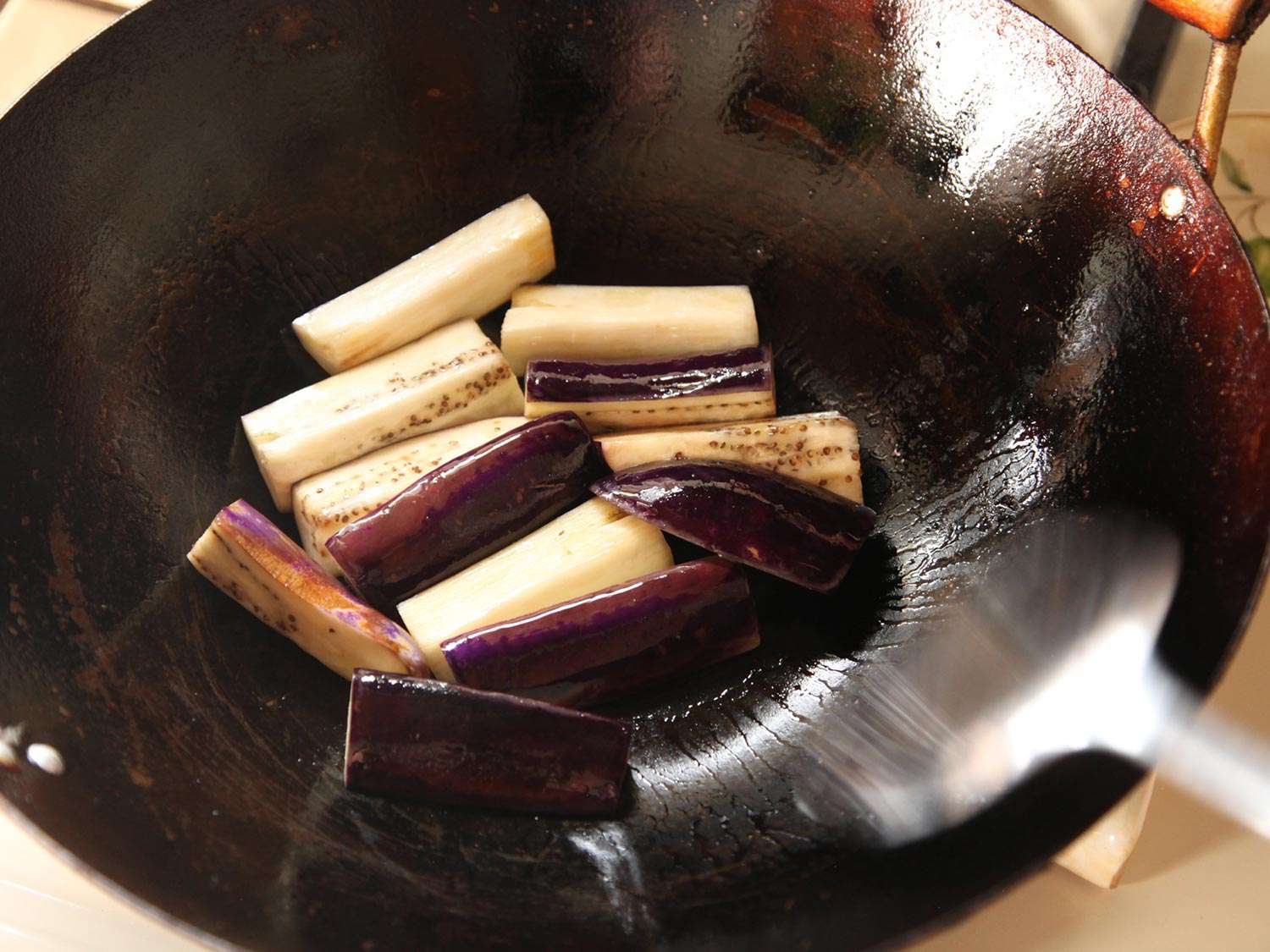 Brined eggplant is stir-fried in a wok.