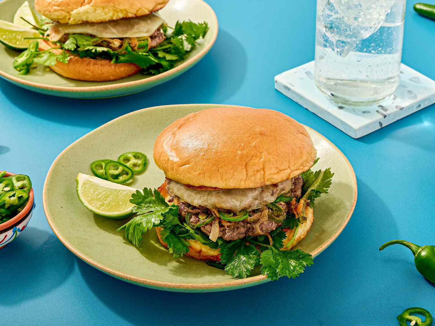 A plated burger with fresh herbs and lime wedges, a glass of sparkling water nearby