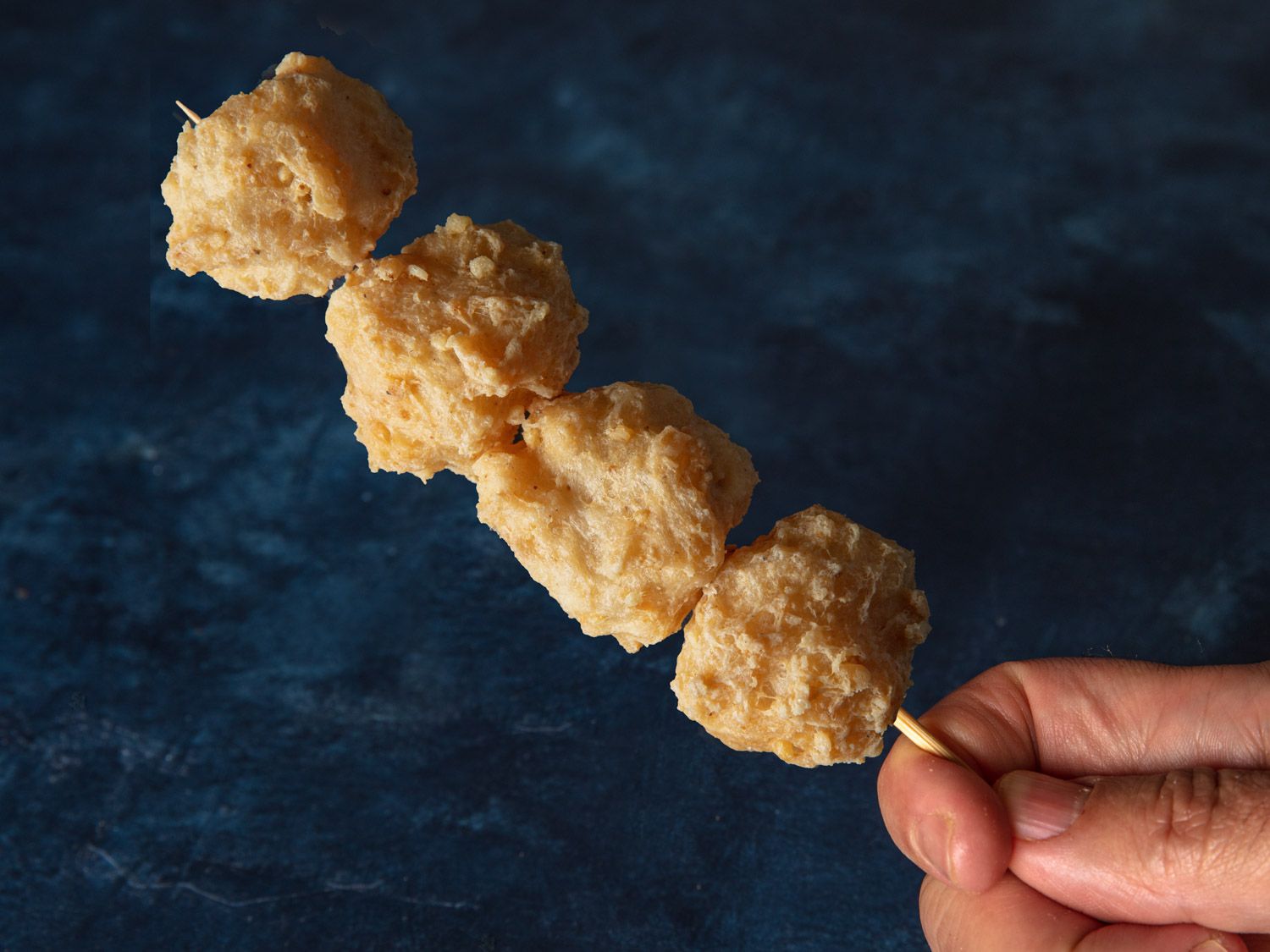 A hand holding a skewer of 4 squid balls.