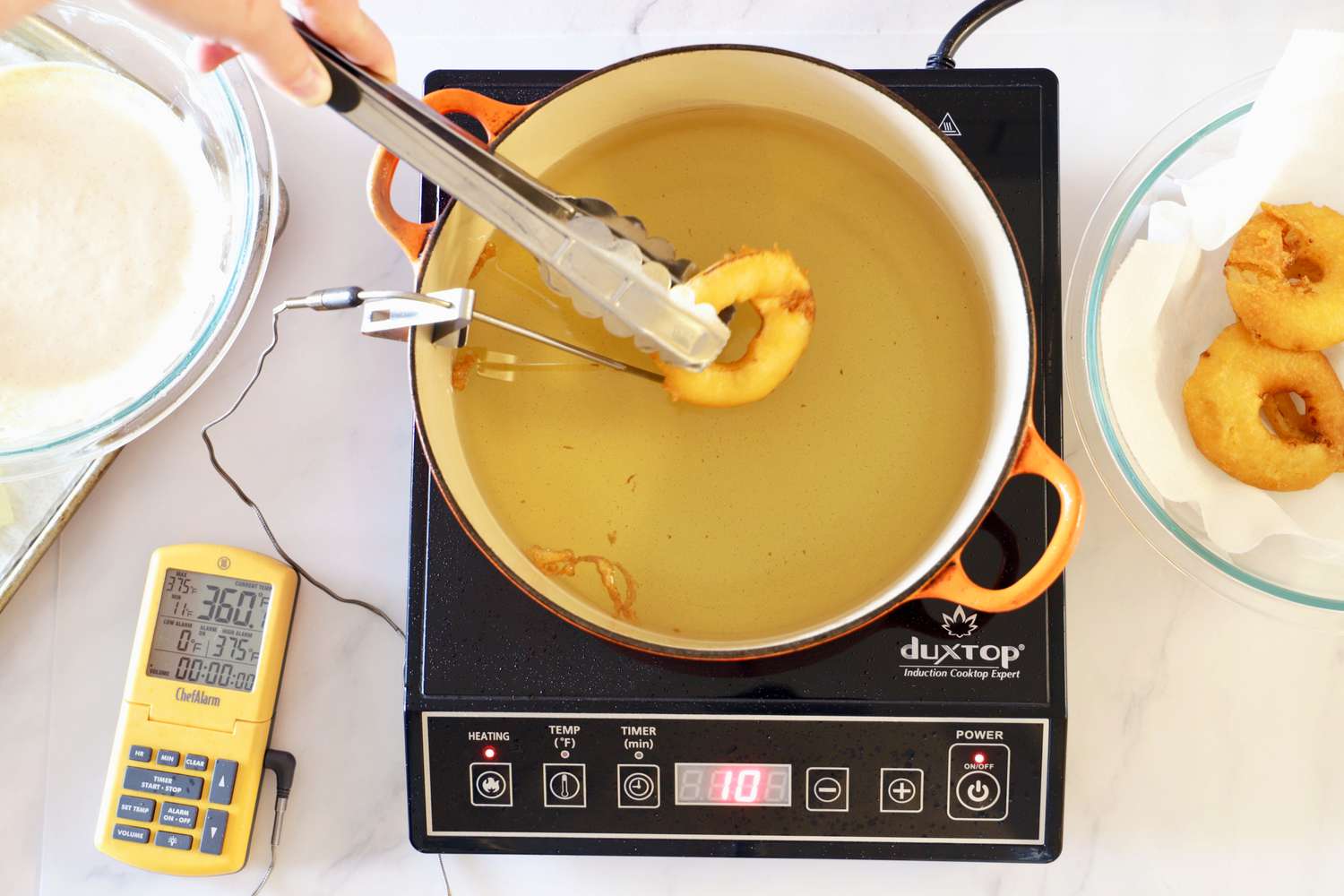 Donuts being fried in a Dutch oven set on an induction cooktop.