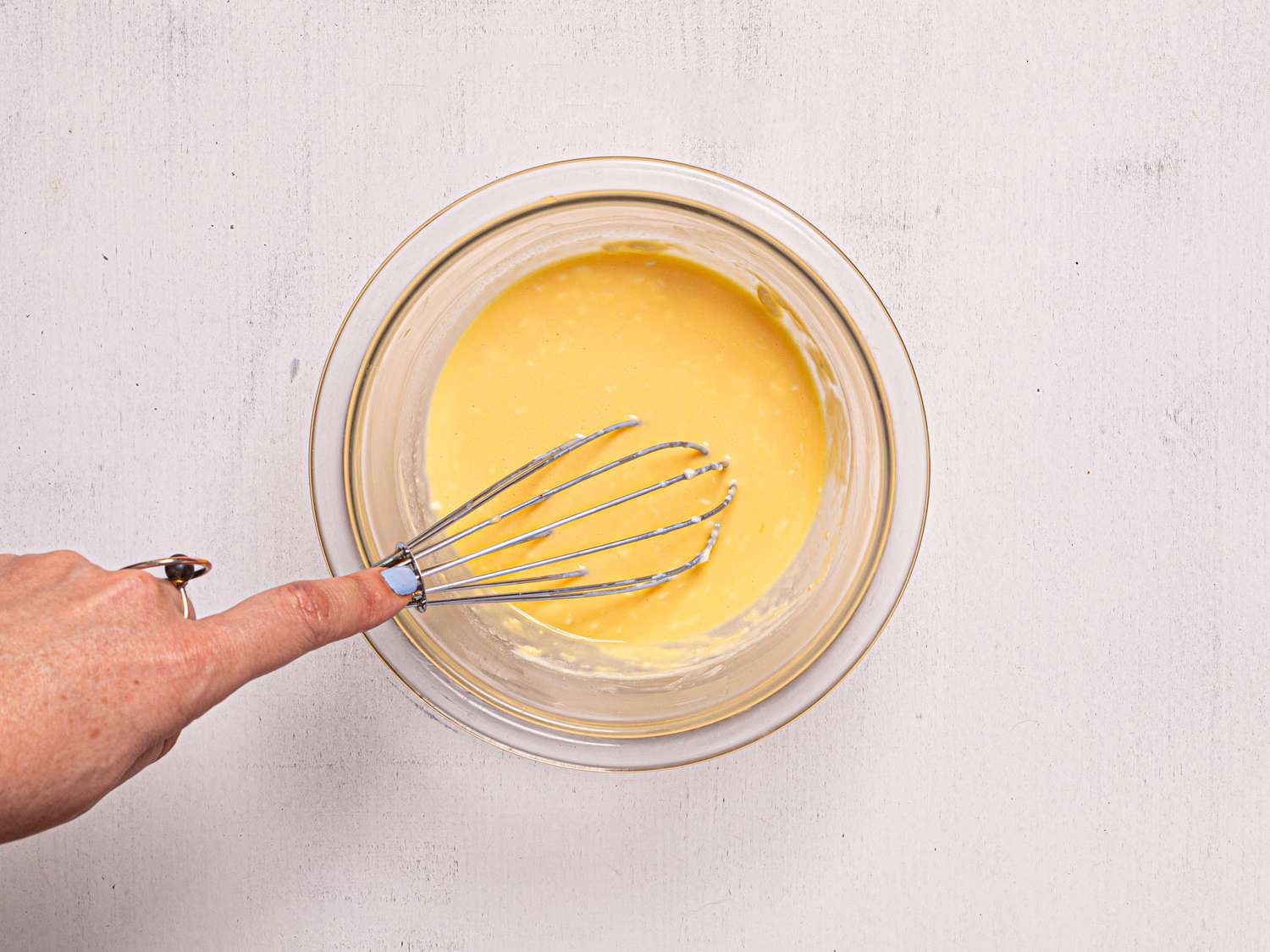 Hand whisking a yellow mixture in a bowl.
