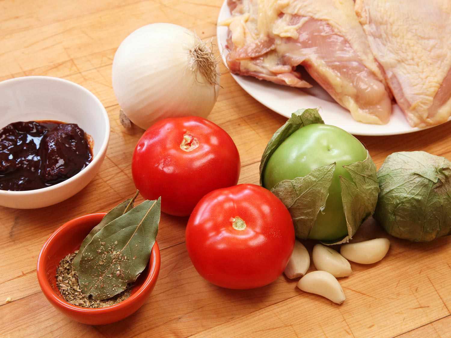 Ingredients for chicken tinga: chicken breast, tomatoes, tomatillos, onion, garlic, bay leaves, dried oregano, and chipotle chiles.