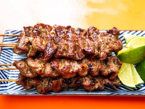 Thai-style grilled pork skewers on a rectangular platter with lime wedges 