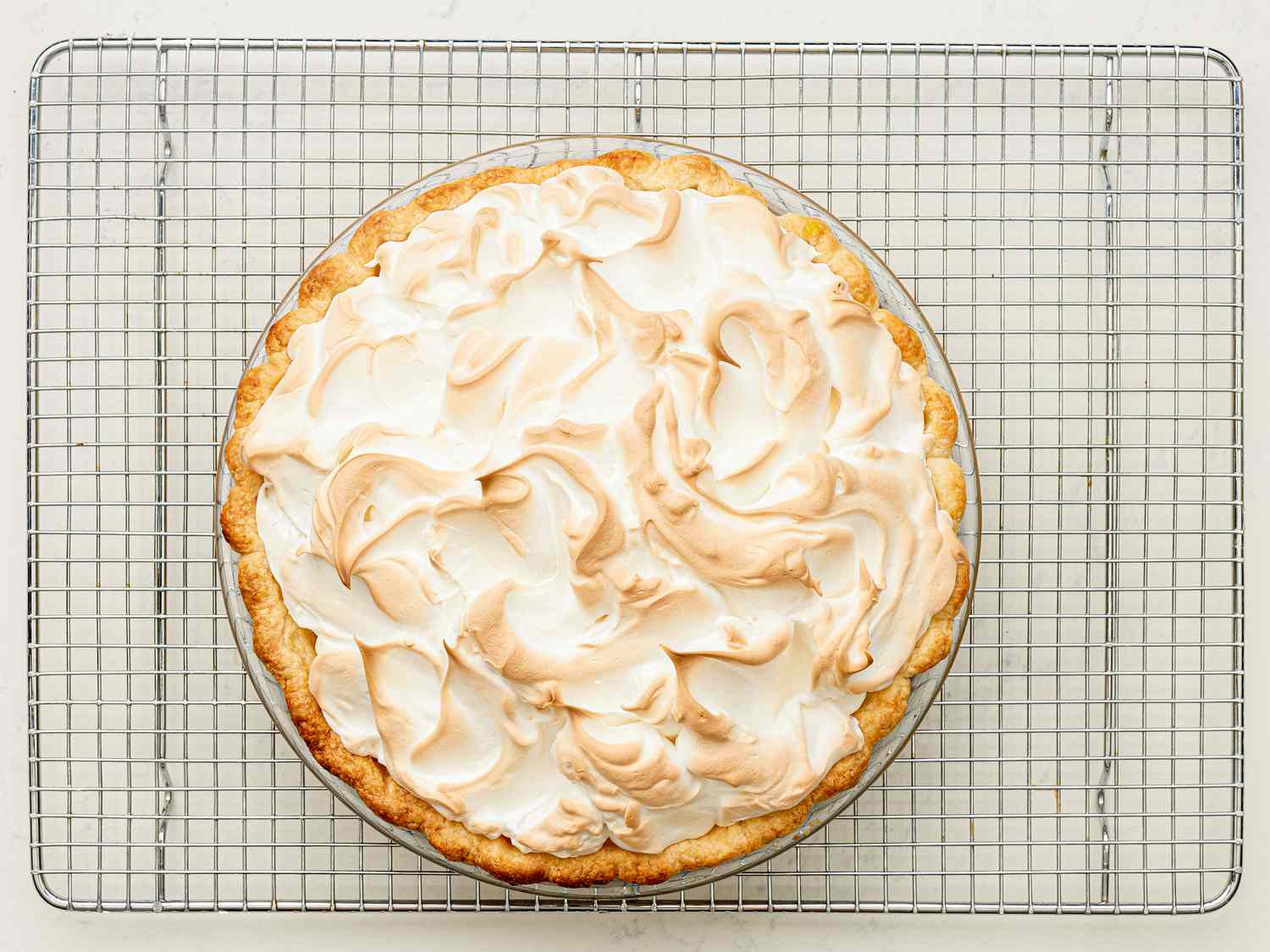 Overhead view of finished lemon meringue pie on a cooling rack.