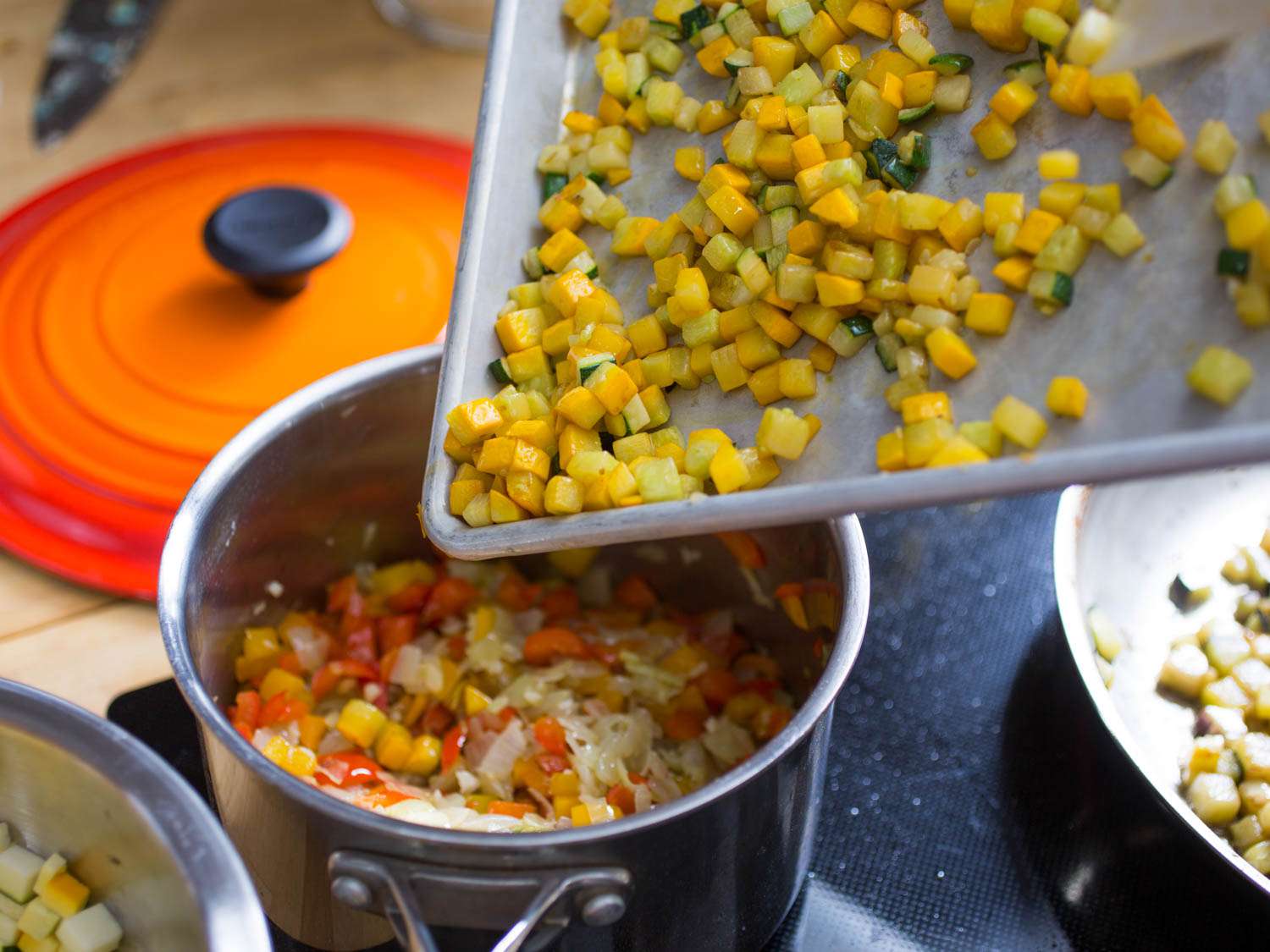 Cooked, cooled summer squash being transferred from the rimmed baking sheet to a saucepan.