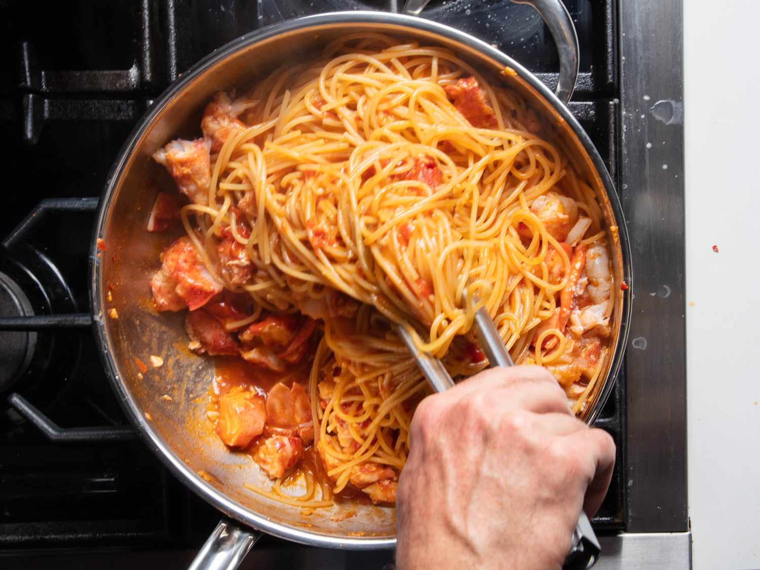 Lobster meat being folded into the pasta in the pan with tongs.