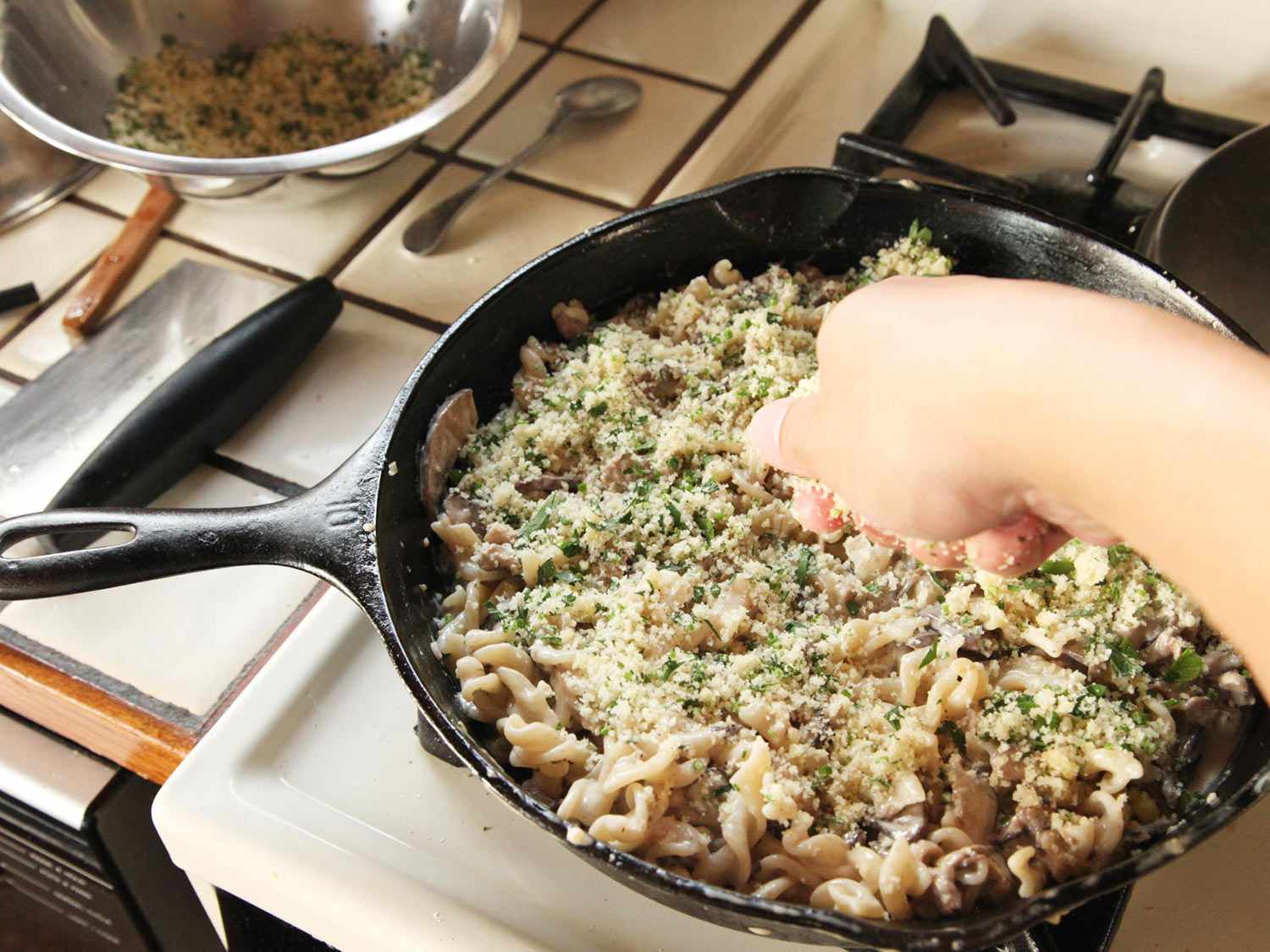 Adding a layer of breadcrumbs over pasta and sauce.
