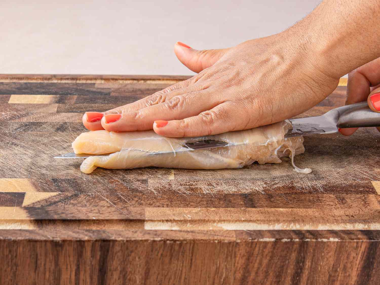 Slicing a raw chicken breast on a wooden board with a knife