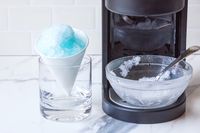 Shaved ice in a cone and a glass bowl with a spoon beside Hawaiian Shaved Ice HomePro Shave Ice and Snow Cone Machine (S777)