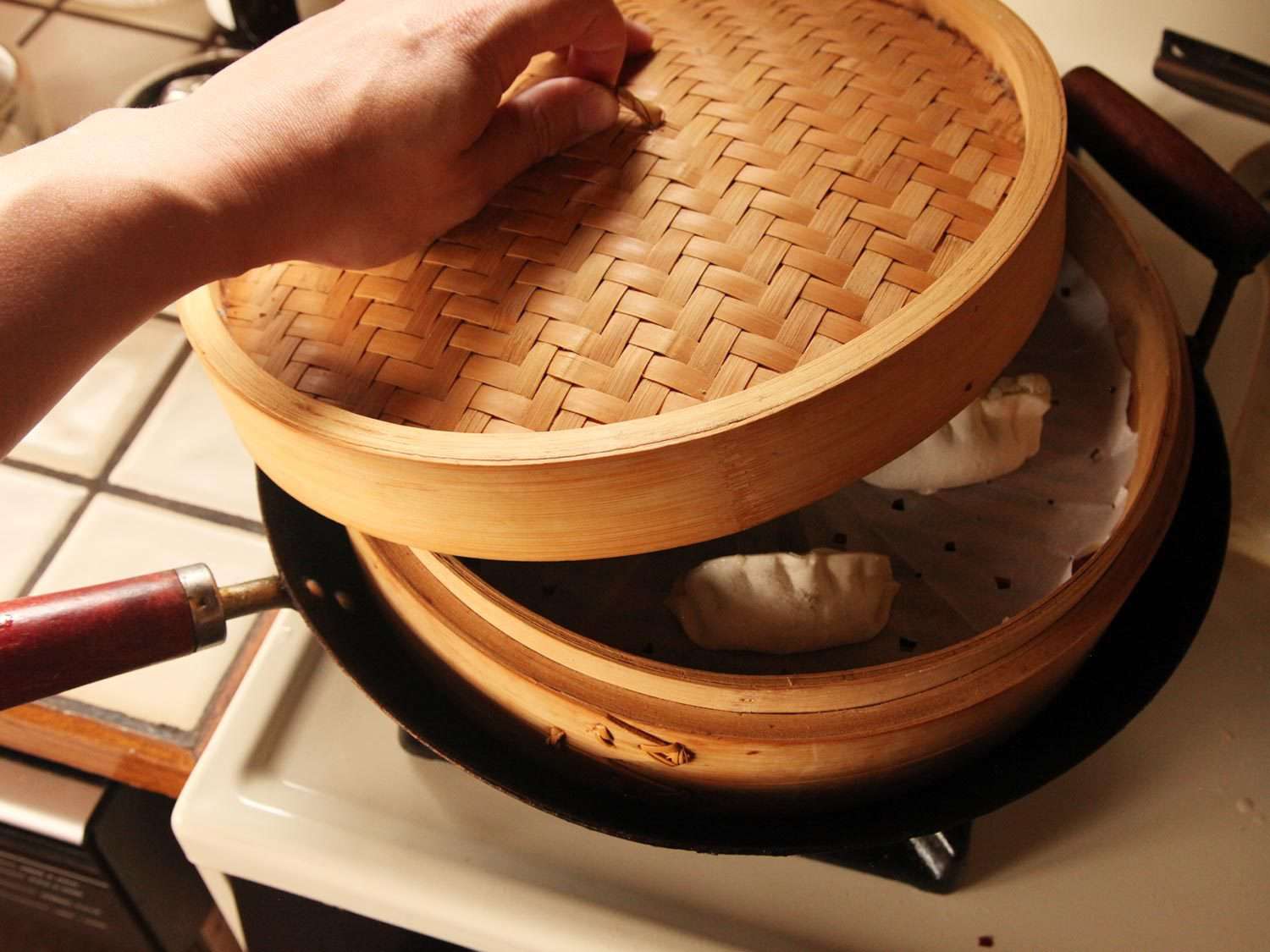 Putting lid on steamer basket with dumplings inside.