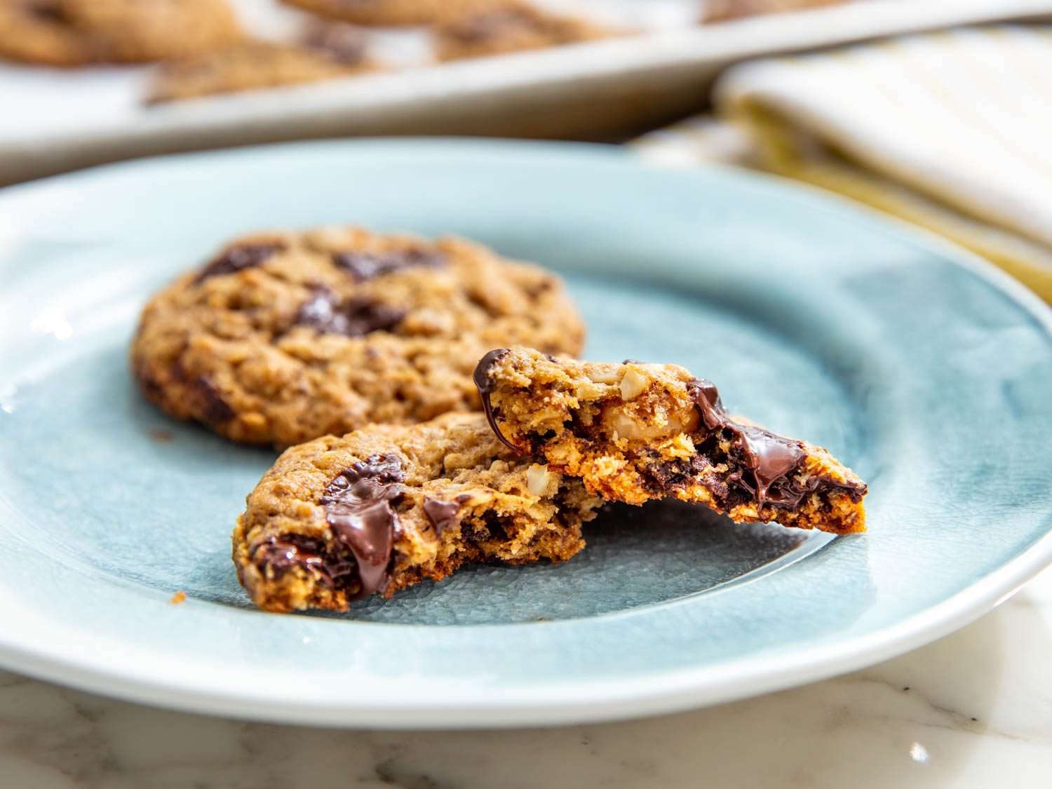 Two vegan lactation cookies on a plate, one broken in half to reveal its hearty texture.