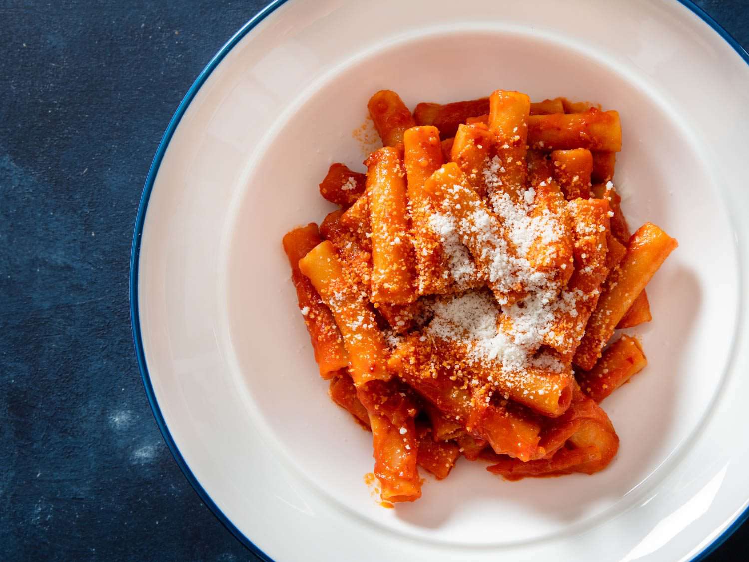 Overhead closeup of an individual serving bowl of pasta with 'nduja tomato sauce, topped with grated cheese.