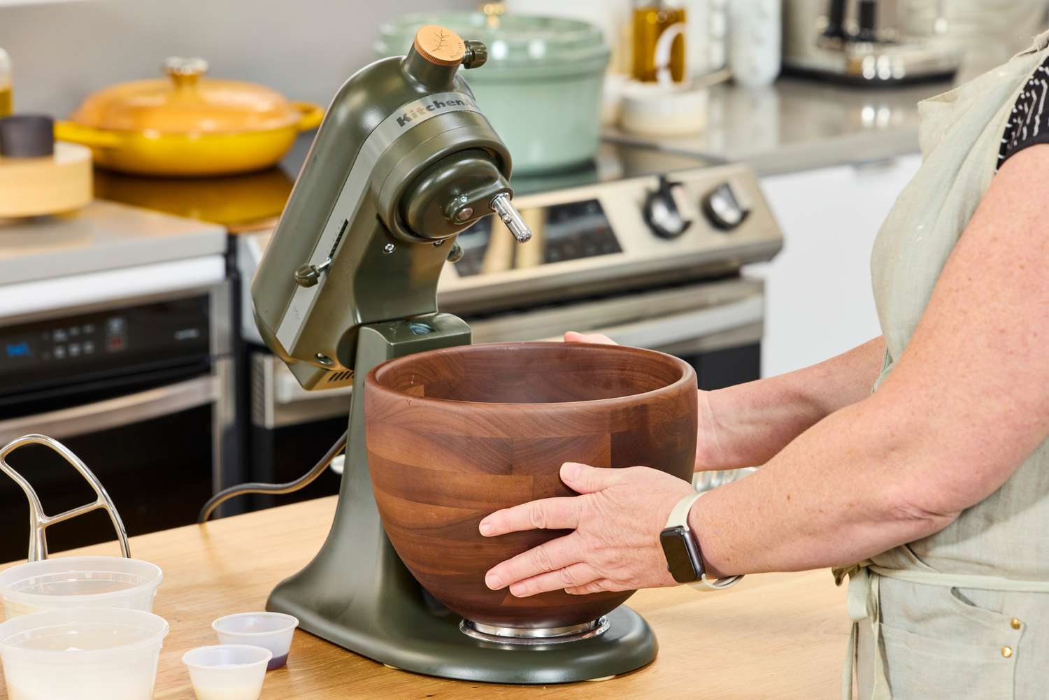 A person places a wooden bowl into the KitchenAid Design Series Evergreen Stand Mixer