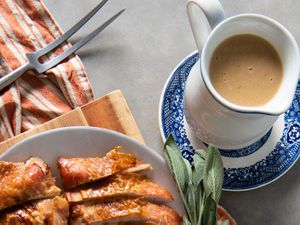 Pitcher of gravy on a blue and white plate next to a platter of roast turkey.