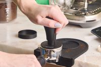 A person using the Normcore tamper to level espresso grounds in a portafilter.