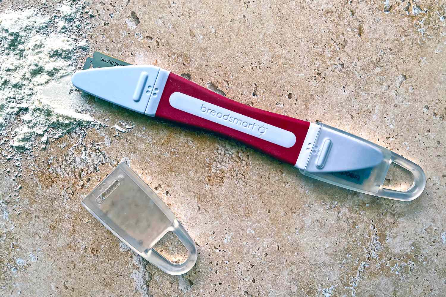 The Breadsmart bread lame on a countertop next to a pile of flour
