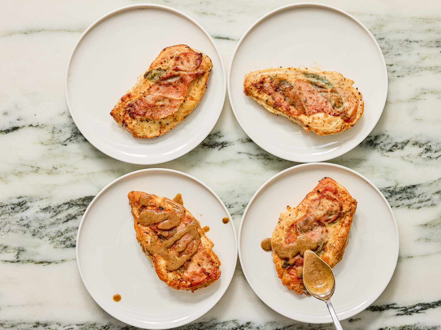 Four plates each holding a portion of chicken saltimbocca textured with sauce arranged neatly on a marble surface