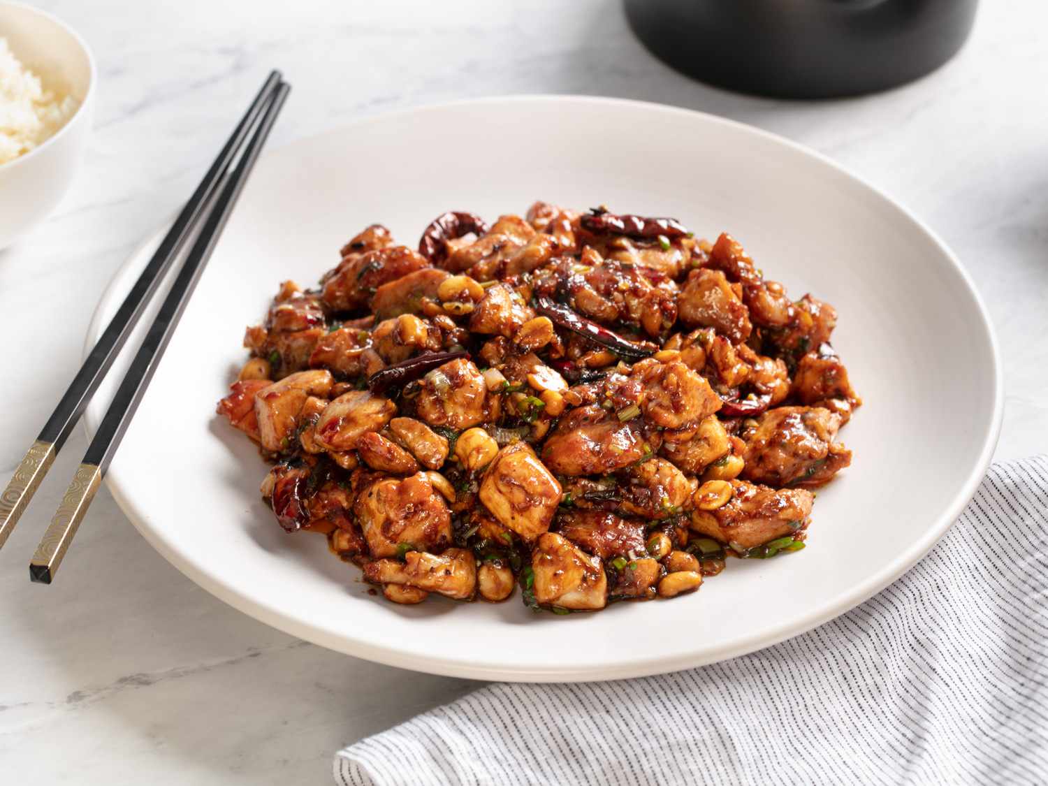 A plate of real-deal kung pao chicken with chopsticks on the side of the plate. 