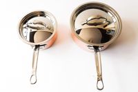 Two saucepans with lids side by side on a white background