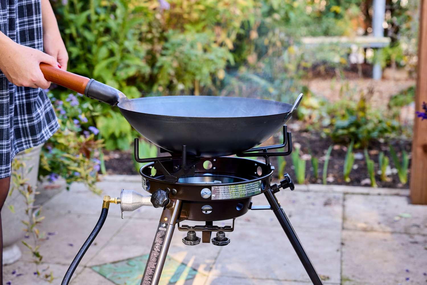 A person placing a wok onto an outdoor wok burner.