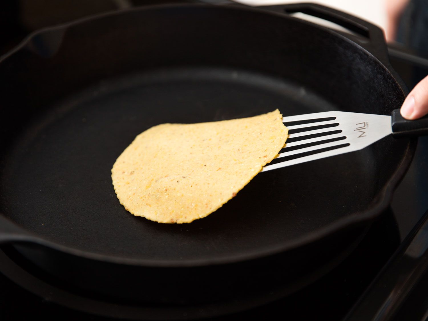 Flipping a homemade corn tortilla in a cast iron skillet