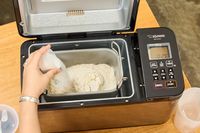 A person adding ingredients into the Zojirushi Home Bakery Virtuoso Plus Bread Maker