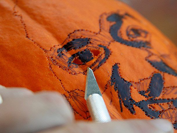Using an X-ACTO knife to carve the design of a face in a pumpkin