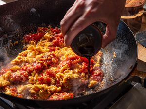 Ingredients being cooked in a pan with a liquid being poured in by hand