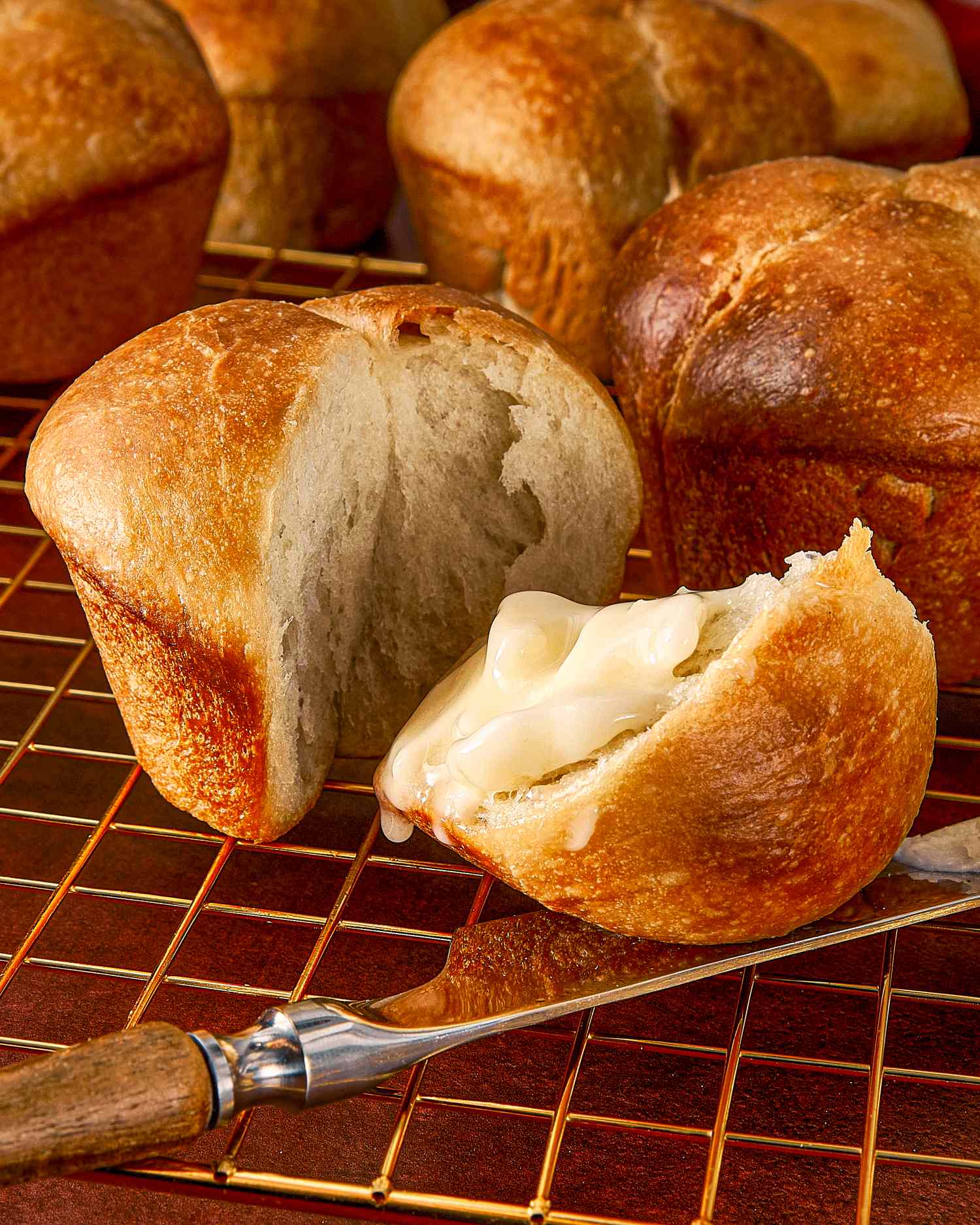 Fresh baked rolls with one cut open and spread with butter arranged on a cooling rack