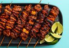 A black platter of charred al pastor skewers and a pile of lime wedges for last-minute drizzling.