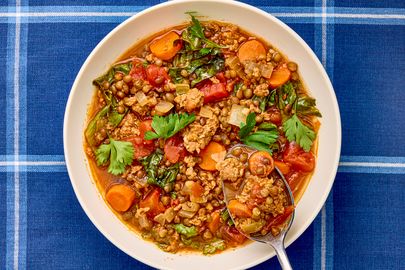 A bowl of sausage and lentil soup with vegetables garnished with parsley on a blue plaid tablecloth
