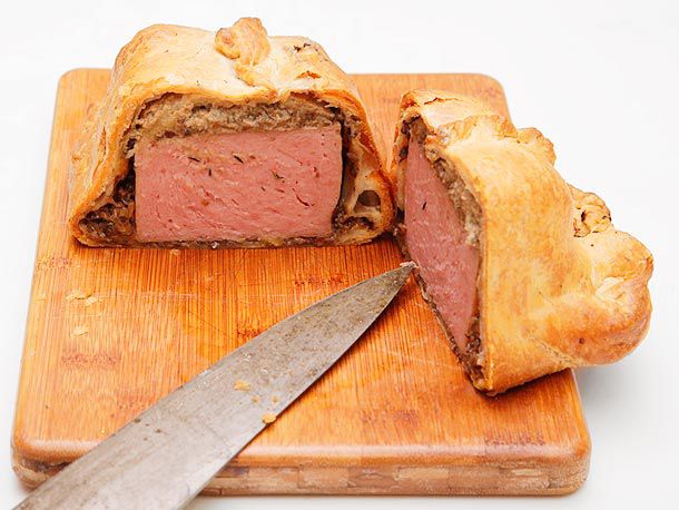 Profile view of a Spam Wellington, halved on a cutting board and angled to show the spammy interior.