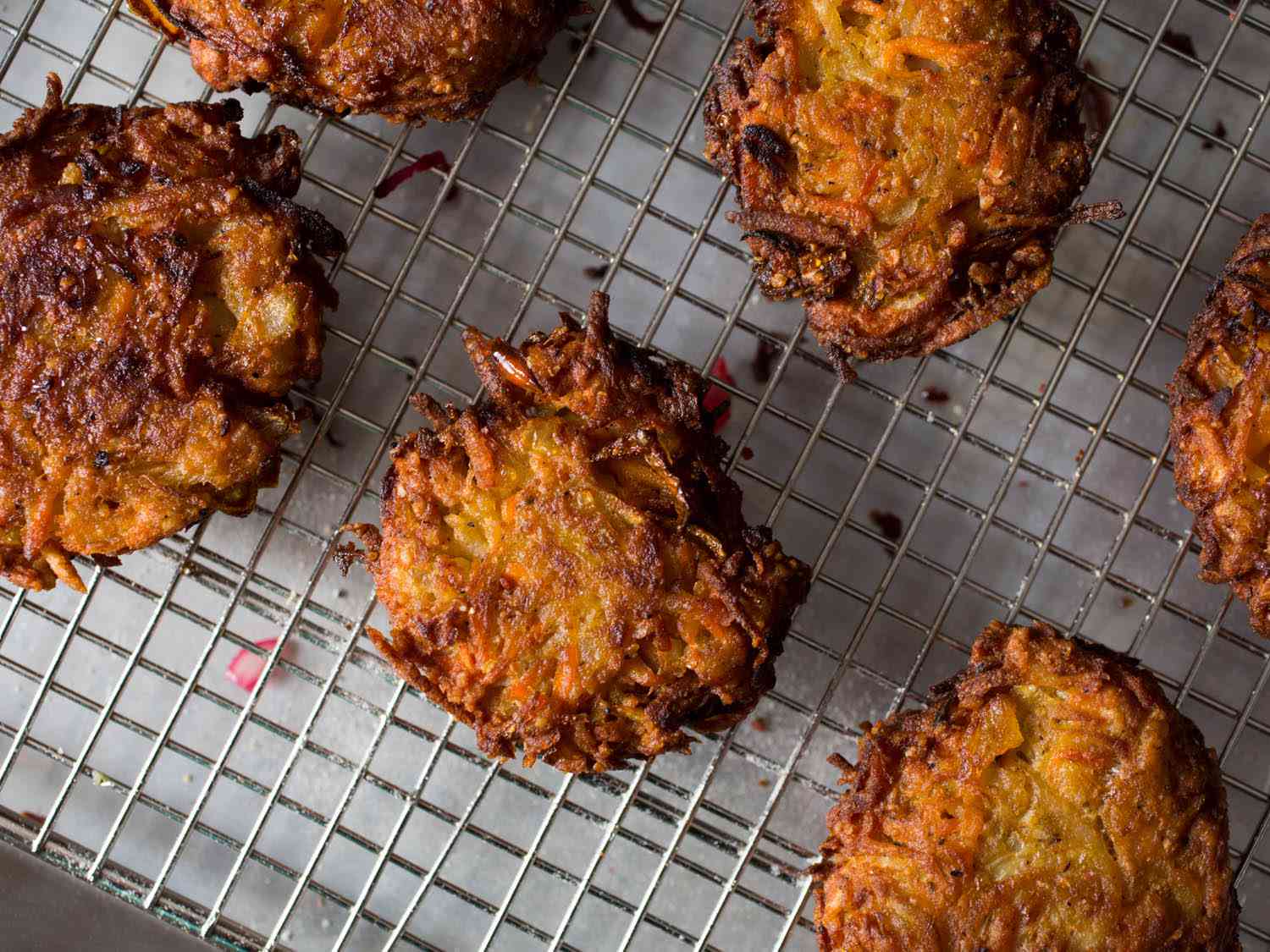 Fried sweet potato, squash, and carrot latkes resting on a wire rack