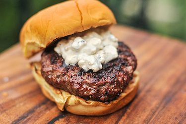 Closeup of a grilled burger topped with chunky blue cheese sauce.