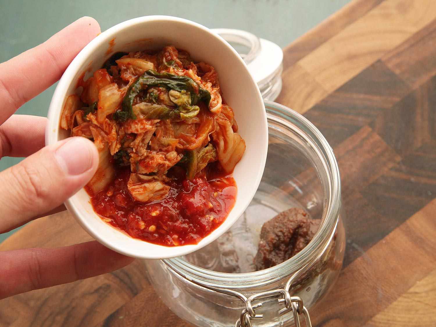 A bowl of kimchi and chile garlic sauce is tipped over the clip top jar.