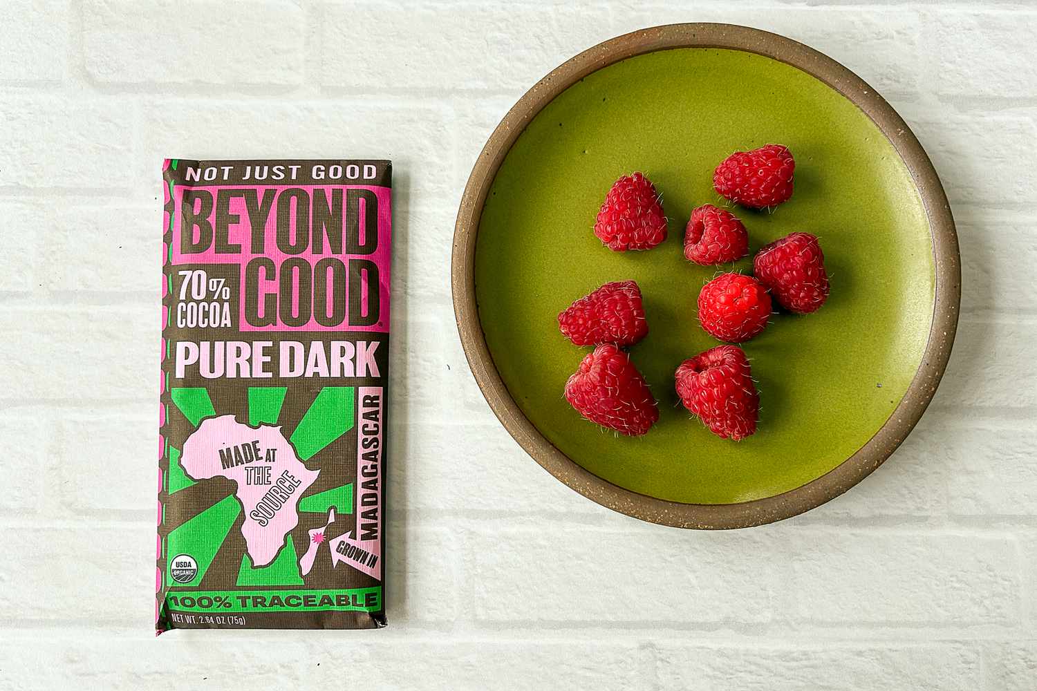 A bar of Beyond Good Pure Dark 70% next to a plate of raspberries