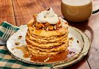 Stack of apple pie pancakes on white rustic plates, a green checked napkin, and warm drink