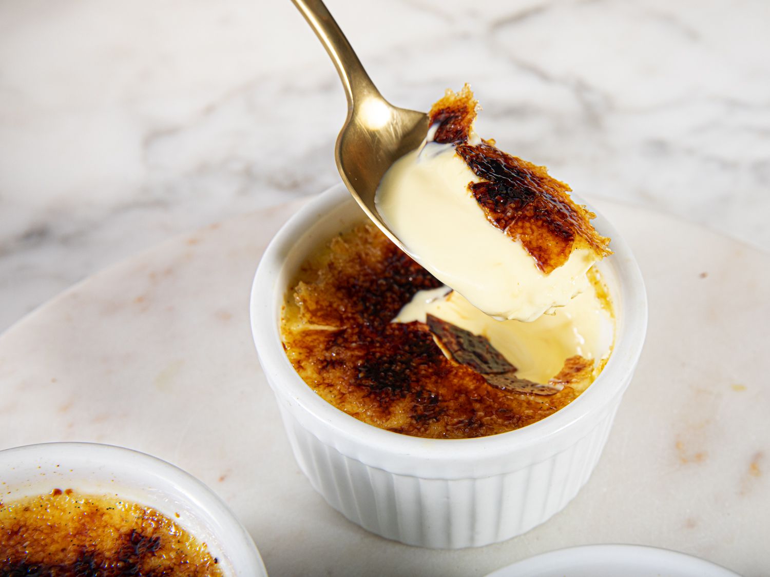 Side angle view of a spoon lifting upa section of creme brulee