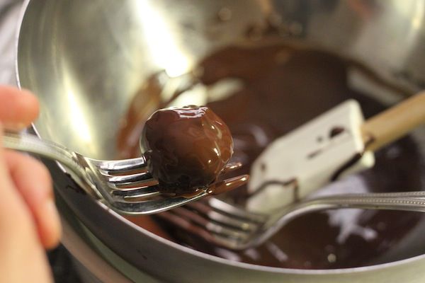 lifting dipped truffle out of a bowl of tempered dark chocolate