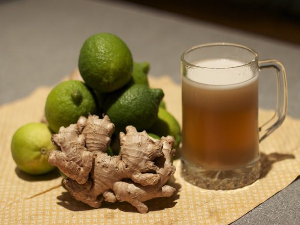 Stein of ginger beer displayed on straw mat with fresh ginger and limes