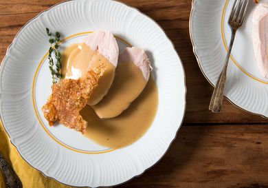 Sliced sous vide turkey breast with crisp skin cracklings and gravy on a white plate.